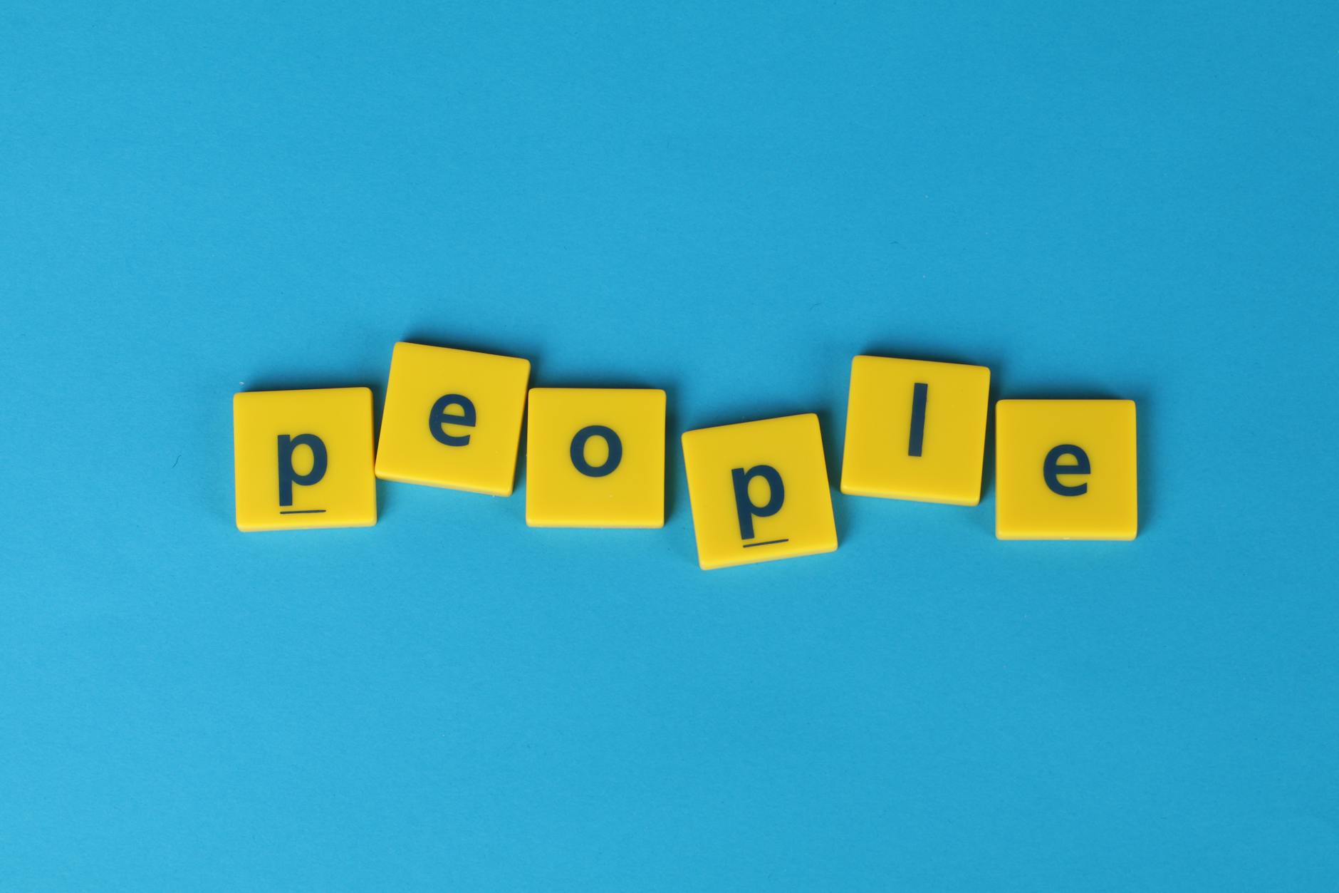 Żółte płytki Scrabble układające się w słowo people na niebieskim tle