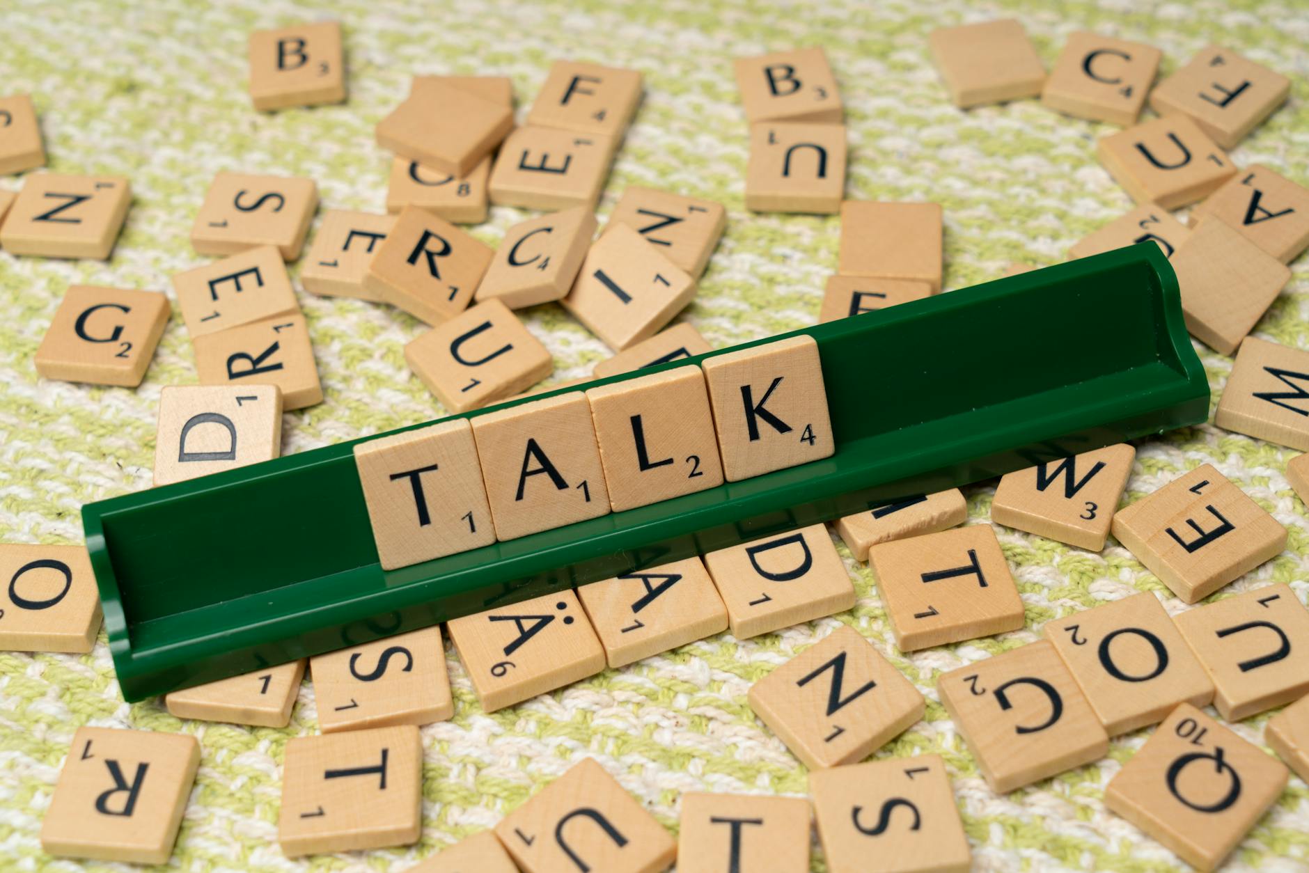 Kafelki Scrabble układające się w słowo Talk na zielonej podstawce