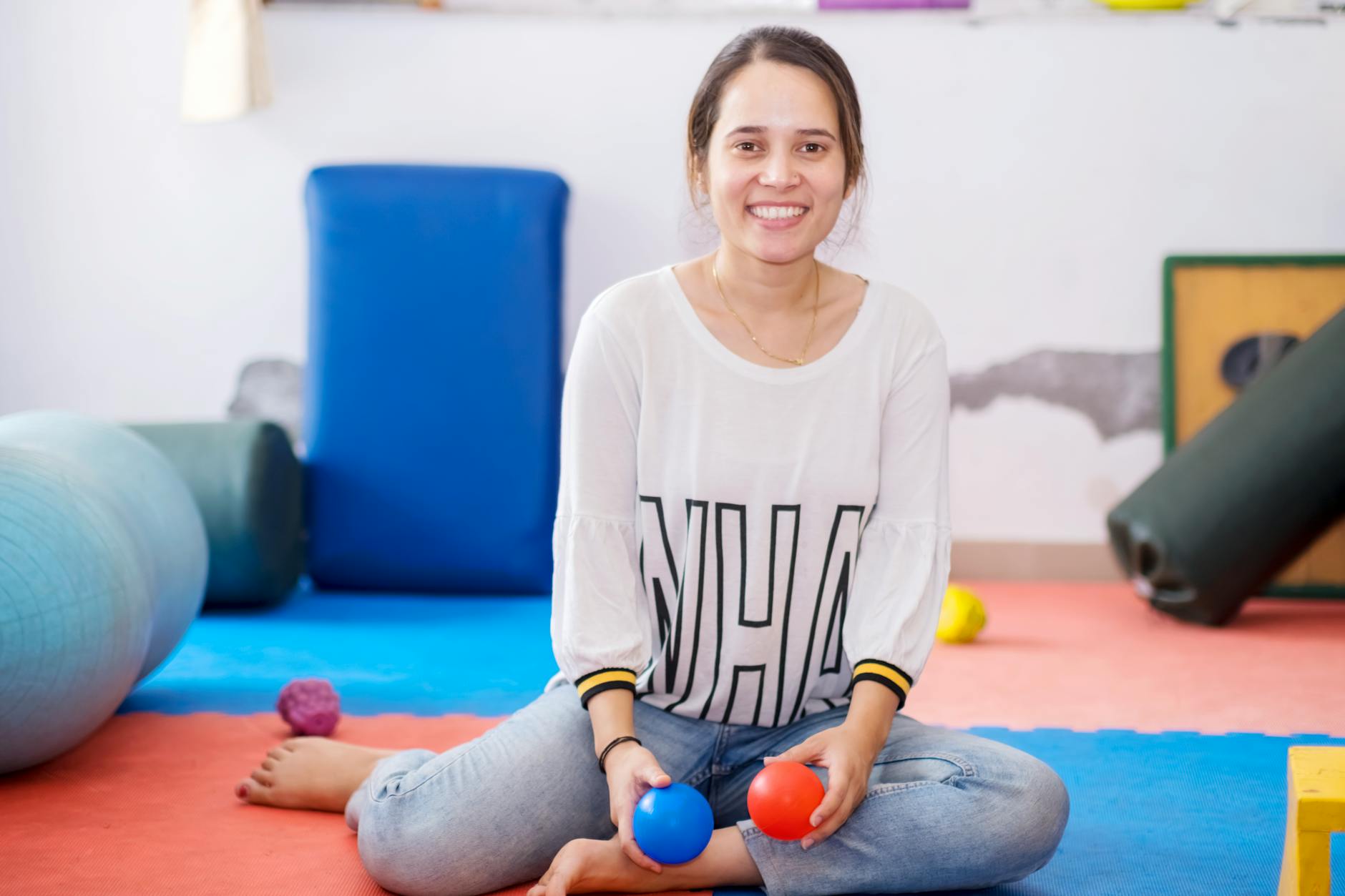 Uśmiechnięta terapeutka trzyma piłki w kolorowej sali do ćwiczeń głosek K i G