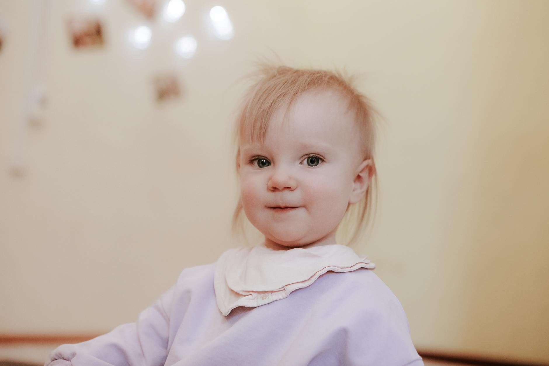 Uśmiechnięta mała blondynka w śliniaku siedząca w domu